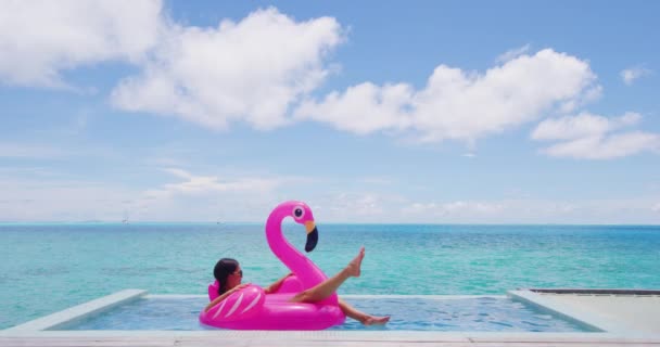 暑假穿比基尼的女人在游泳池里躺在充气粉色火烈鸟玩具床垫上。优雅的女士在度假胜地享受假日日光浴.奢华的生活方式.