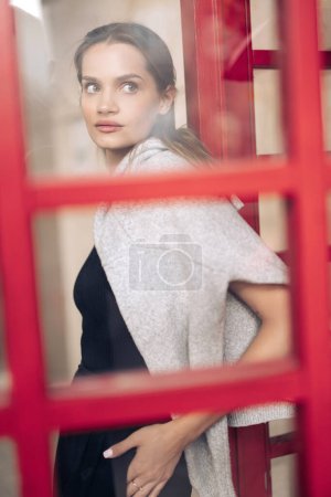身穿黑色衣服的年轻漂亮女子在大楼的背景下进入红门。穿上衣服透过玻璃看.
