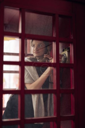 透过玻璃窗，在收费电话亭里给年轻女子拨打电话号码。包扎.