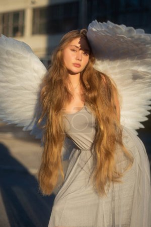 美丽的女孩，长长的金发。一个长着大翅膀的天使女孩站在太阳前。阳光照射在天使身上