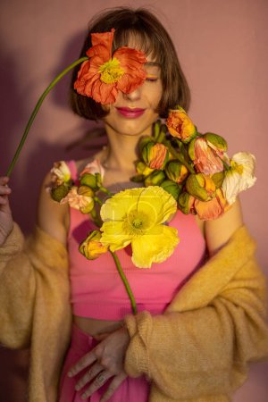 一个年轻女子的画像，她有一株粉色背景的岛上罂粟切花。美丽与夏天的概念