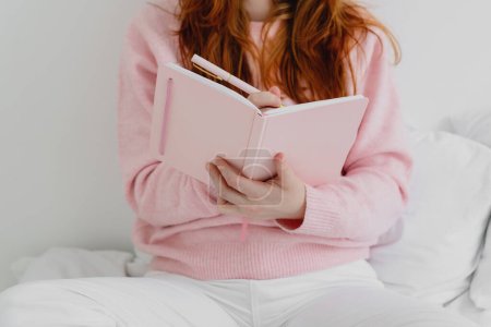 红头发女人坐在床上并在笔记本上写下的剪下来的图片.