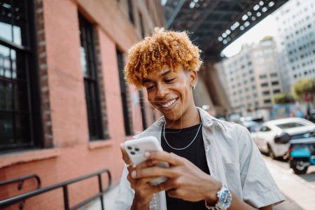 年轻的多种族男子在城市散步时，用智能手机开心地微笑的画像。一个人走在空荡荡的街道上享受周末